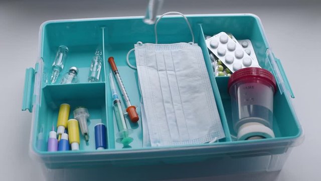 Hand in medical gloves puts a syringe and ampoules with medicine in first aid kit, slow motion. Healthcare and virus protection concept