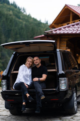 Portrait of beautiful sexy blonde woman and man sitting in luxury dark car . Fashion and business concept. Idea for couple photoshoot with car. Valentines day, surprise.