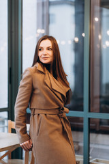 Outdoor fashion portrait of stylish young woman having fun, emotional face , laughing, Urban city street style wearing dark casual trousers, white sweater,creamy coat. and sunglasses Fashion concept.