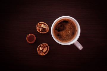 Top view of a white Cup with black coffee, a walnut and one sweet candy with hazelnut