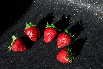 5 strawberries on a black background. Berries on a shiny black table.