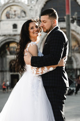 happy bride and groom cuddling while walking around the old city of venice,groom of Georgian appearance hugs a bride of European appearance,european wedding,lovely wedding couple look at each other
