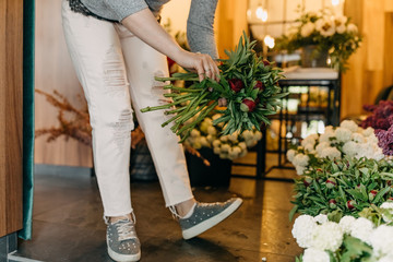 Woman picking peony flowers for a bouquet form a bucket in flower shop.