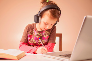 Distance learning online education. Young child  girl in headphones studies at home and does school homework with laptop.