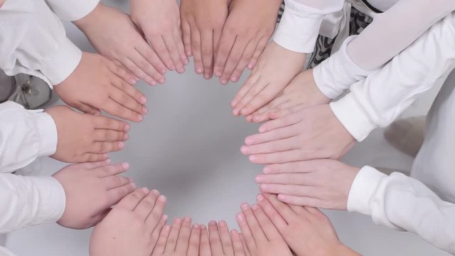 Children hold their hands in an educated circle with palms down on a white background.