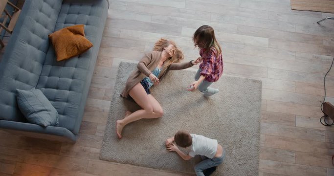 Top view young happy Caucasian mother dancing round with two cute kids, hugging and going crazy on vacation at home.