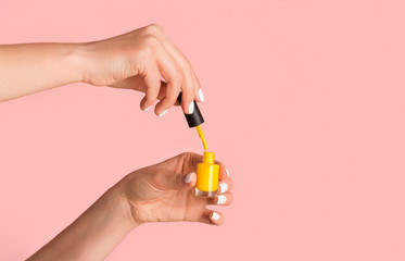 Close up of nail artist holding bottle of yellow enamel on pink background, copy space - obrazy, fototapety, plakaty