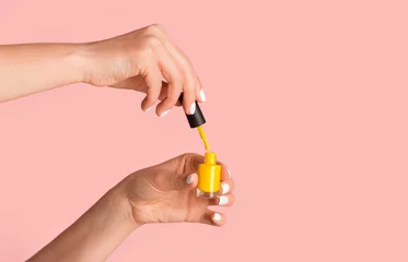 Poster Close up of nail artist holding bottle of yellow enamel on pink background, copy space © Prostock-studio