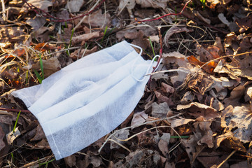 White disposable medical mask on dry leaves. Thrown face mask like trash. Environmental pollution during the pandemic