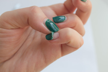 Damaged female nail with green manicure. Peeled off gel polish with nails. Home manicure concept