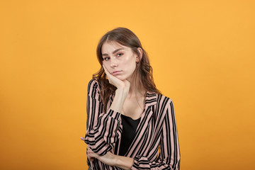 Cute Young Woman Light Brown In Striped Pink And Black Shirt On A Yellow Background, Sad Girl Hesitates To Make A Decision, Leaned Her Head On Her Hand