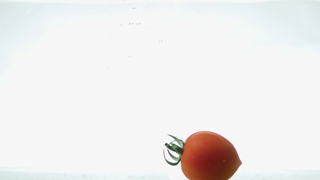 Single tomato falling into water on white background