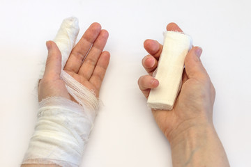 a left hand with an injured index finger bandaged and a right hand holding a white bandage, two...