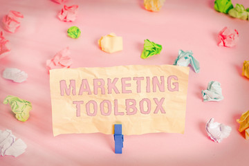 Writing note showing Marketing Toolbox. Business concept for Means in promoting a product or services Automation Colored crumpled papers empty reminder pink floor background clothespin
