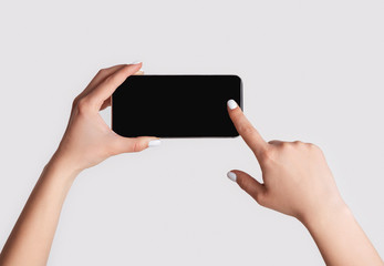 Closeup of woman touching mobile phone with blank screen on light background, copy space
