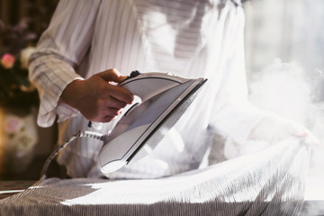 Close up hands of senior woman ironing clothes using steam. Steaming washed laundry. Visiting mom. Home chores of an elderly person. Self-isolation for the elderly