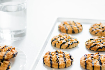 Side view oatmeal cookies covered with chocolate, a glass of water in a white dish on a white background. Concept of cooking Breakfast and baking at home