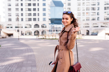 Cheerful fashionable young woman taking cup of coffee outdoors walking