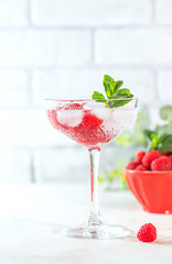 Raspberry lemonade with mint and ice in a glass on a light concrete background.