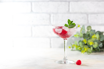 Raspberry lemonade with mint and ice in a glass on a light concrete background.