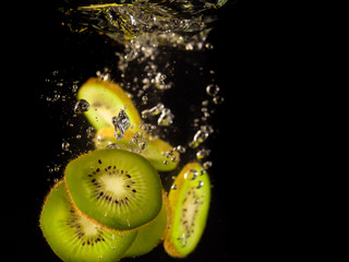 Closeup of fresh kiwis slices falling into clear water with big splash on black background. Group...