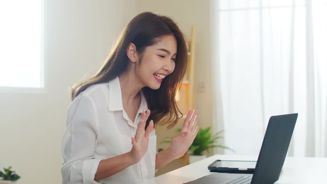 Young Asian business female using laptop video call talking with couple while working from home at living room. Self-isolation, social distancing, quarantine for coronavirus in next normal concept.