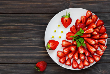 Strawberries on a white dish, red, juicy strawberries cut into slices, decorated with a sprig of mint. Cooking concept, brown wooden background with copy space for text.