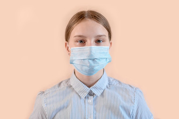 Teenager girl 15 years old, in medical mask covers her face, beige background, COVID-19 sars-cov-2 epidemic pandemic virus outbreak protection concept
