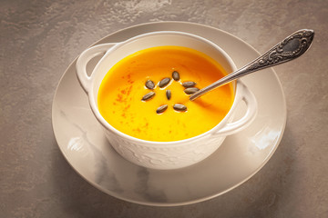 Bowl of tasty pumpkin soup and space for text on gray table, top view.