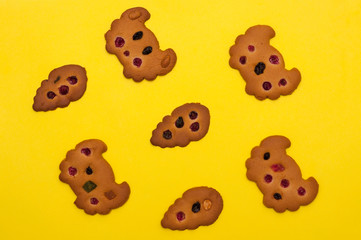 Top view of homemade cookies decorated with berries, raisins and colored candied fruits at yellow background