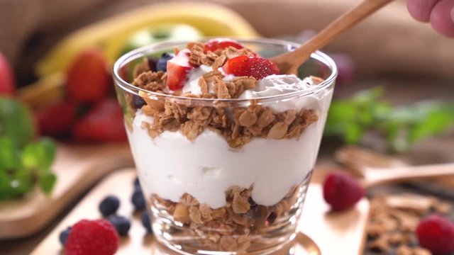 Scooping Yogurt with granola and fruits .	