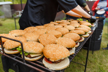 A lot of burgers lie on the grill. Catering food preparation for outdoor party. Barbeque for big company © bearmoney