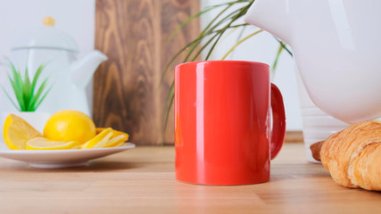 Hot coffee pouring to red cup on oak table. Close up.