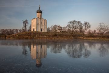 Obraz premium A beautiful temple on a background of bright golugobo sky stands on the shore of a lake is reflected in the ice at sunset