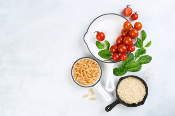 Food background with vine tomatoes, spinach leaves, white rice, fusilli pasta and cast iron skillet. Background, top view, banner. Vegan, diet food concept. Composition with ingredients for cooking.