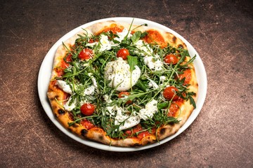 Pizza with mozzarella, tomato,arugula, thin dough, on plate. Brown background, top view