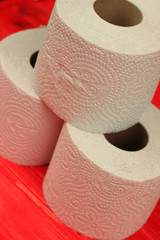 Three rolls of white toilet paper on red background with space for text. Deficit means of hygiene...
