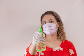 Mujer latina con vestido rojo tomando precauciones por el Covid-19 usando una mascarilla, guantes y un atomizador con alcohol para prevenir infección del coronavirus en el 2020