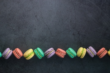 Colourful minimalistic greeting card concept. Different colours macaroons on black grunge stone...