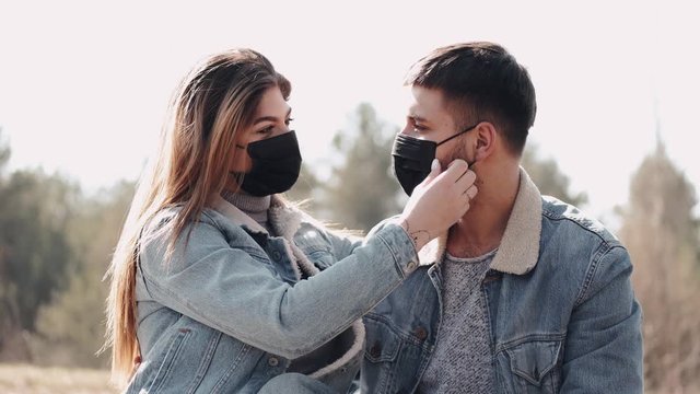 A young handsome and a woman are on a date. A couple in masks is kissing at sunset in the field. They are wearing protective masks during quarantine.