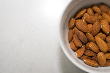 A white bowl of almonds on a white background with copy space