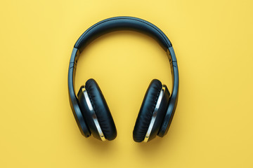 Photo of black stylish modern wireless headphone in neon lights over yellow background.