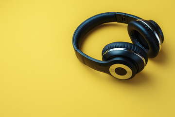 Photo of black stylish modern wireless headphone in neon lights over yellow background.