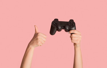 Stay home hobbies. Millennial girl showing video game joystick and thumb up gesture on pink...