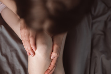 Top view cropped images of unrecognizable woman with knee pain, young woman massaging her painful knee sitting on bed at home, Health care concept. Selective focus