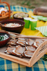 Ukrainian picnic outdoors. Sliced ham, dark ceramic, bread, greens, sweets, salad at sunset in the park