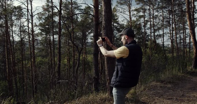 A young man takes a photo with a your phone in the woods. Man take selfie in beautiful mountains in autumn , sumer time.