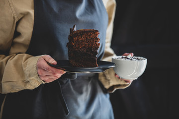 woman in an apron holds cappuccino and chocolate cake
