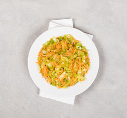 Cabbage salad with carrots on a plate on a light background top view