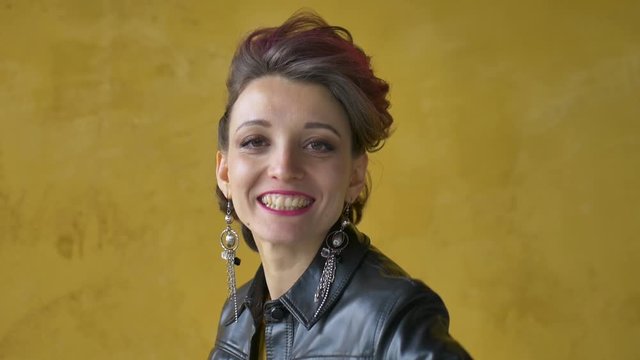 Let's rock concept. Portrait of excited beautiful woman with dark pink hair in casual yellow dress standing, looking at camera, showing rock and roll gesture.